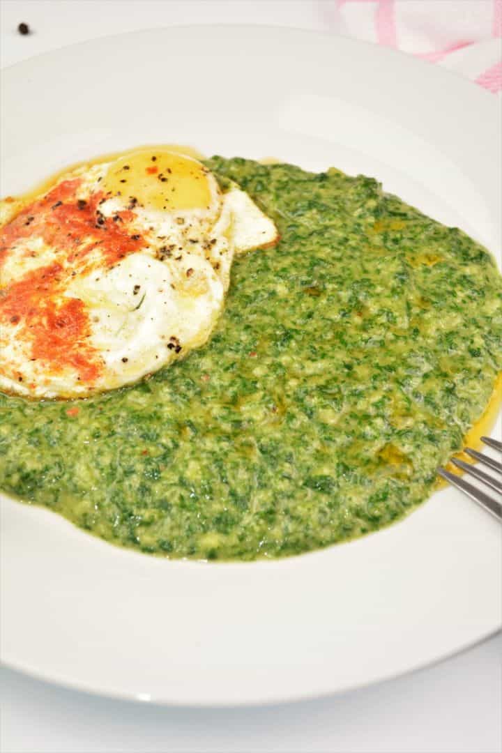 An overhead view of a rustic plate containing the completed quick creamed spinach recipe, topped with a perfectly fried egg with runny yolks and crispy edges, ready to serve with a slice of sourdough bread.