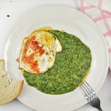 An overhead view of a white plate containing the completed quick creamed spinach recipe, topped with a perfectly fried egg with runny yolks and crispy edges, ready to serve with a slice of sourdough bread.