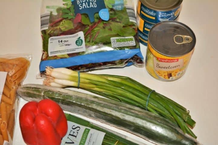 Simple Tuna And Pasta Salad Recipe - Few Ingredients Fresh ingredients for a healthy tuna pasta salad gathered on a kitchen counter, including canned tuna chunks in oil, penne, red bell pepper, and a fresh lemon.
