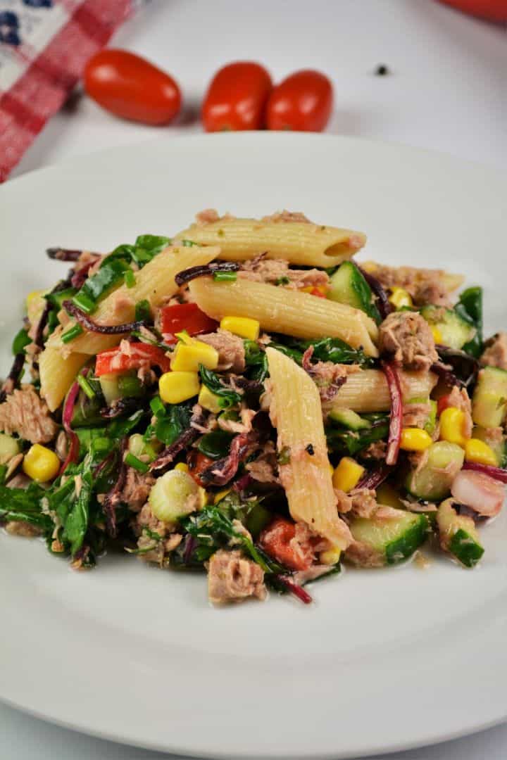 Simple Tuna And Pasta Salad Recipe - Served on Plate A beautifully plated portion of healthy tuna pasta salad without mayo, showing a colorful mix of penne, sweetcorn, crisp red bell pepper, and fresh chives.