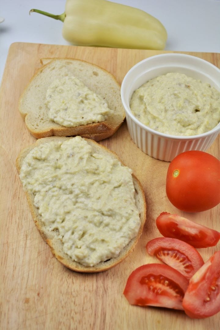 Authentic Romanian Eggplant Dip (Salată de Vinete) served on slice of bread with fresh tomato slices on a wooden table.
