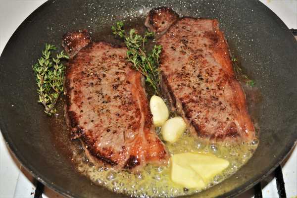 Easy Pan-Fried Steak Recipe-Melting Butter With Frying Steaks, Garlic Cloves and Thyme in the Pan