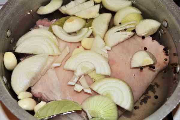 Braised Pork Knuckle Recipe-Sliced Onions, Garlic Cloves, Bay Leaves and Peppercorns Over the Knuckle in the Pot