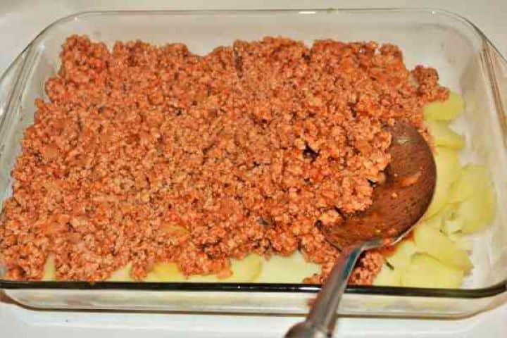 Easy Potato Moussaka Recipe-Fried Pork Mince on the Sliced Potatoes in the Baking Tray Spreading the cooked minced pork filling evenly over the bottom potato layer.