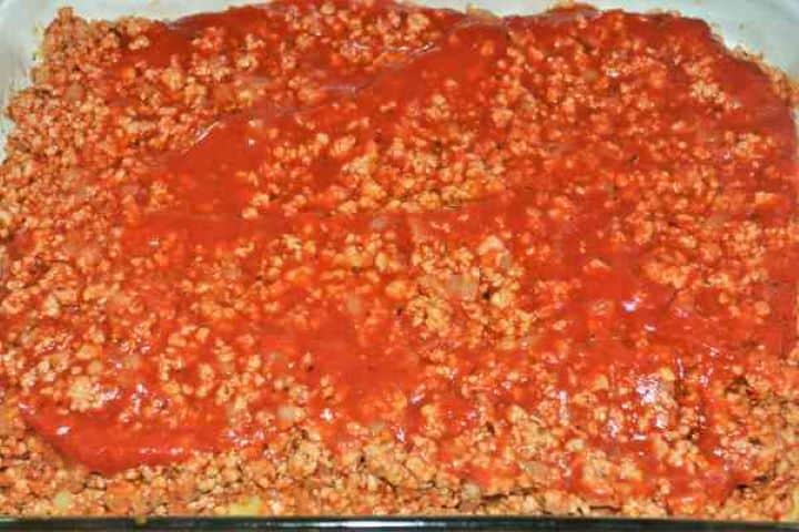 Easy Potato Moussaka Recipe-Pouring Tomato Passata Over Fried Pork Mince in the Oven Tray Drizzling tomato passata over the minced meat layer in the casserole dish.