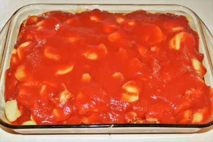 Easy Potato Moussaka Recipe-Pouring Tomato Passata on Top of Baking Tray Pouring tomato passata evenly over the top potato layer before baking.