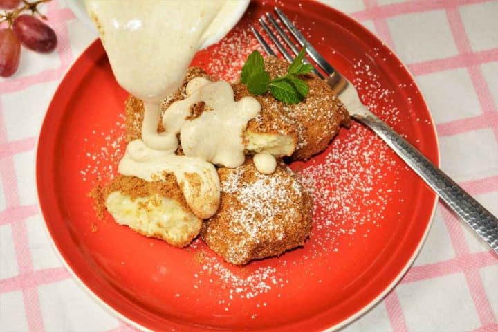 Best Cottage Cheese Dumplings-Pouring Cream Over Served Dumplings on the Plate Spoon pouring sweet vanilla sour cream sauce over warm breadcrumb-coated cottage cheese dumplings.