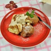Authentic Hungarian cottage cheese dumplings (Túrógombóc) served on a red plate with sweet vanilla sour cream.