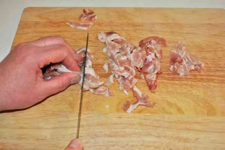 Turkey Cabbage Stew Recipe-Cutting Bacon in Small Pieces Finely diced smoked bacon ready for frying on a wooden chopping board.
