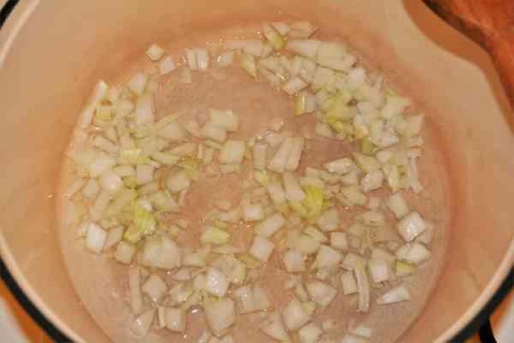 Sautéing finely chopped onion in sunflower oil inside a pot.