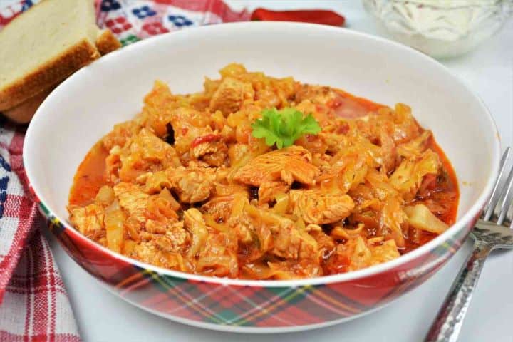Turkey Cabbage Stew Recipe-Served in Bowl With Bread and Sour Cream Homemade Hungarian turkey cabbage stew plated in a deep bowl with sour cream and chili pepper.
