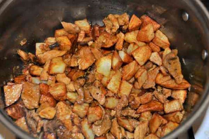 Brasov Roast Recipe-Pork Stew With Fried Potatoes in the Pot A wooden spoon stirring the steaming hot mixture of braised pork and crispy potatoes in the cooking pan.