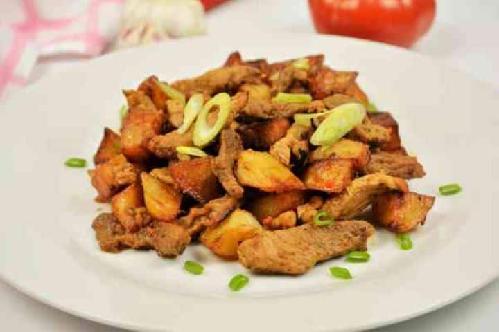 Brasov Roast Recipe-Served on Plate With Chopped Spring Onion on the Top Final plated portion of authentic Brasov roast served warm on a dinner plate, garnished with fresh green parsley.