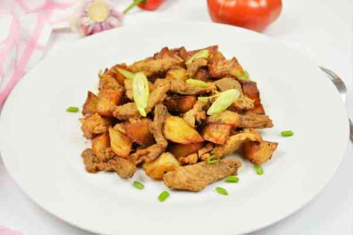Brasov Roast Recipe-Served on Plate With Chopped Spring Onion on the Top Close-up overhead shot of the finished garlic pork skillet meal showing the contrast of tender meat and crispy potatoes.