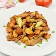 Authentic Hungarian Brasov roast skillet featuring tender garlic pork shoulder and crispy fried potatoes garnished with parsley.