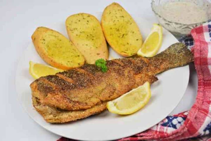 Pan-Fried Rainbow Trout Served on White Plate With Lemon and Garlic Bread