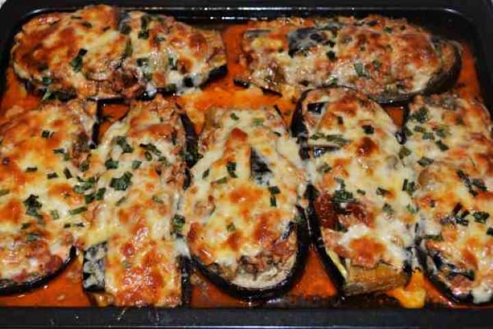 Stuffed Aubergines Recipe-Baked Stuffed Aubergines on Baking Tray Ready to Serve A baking tray filled with golden, copper-colored pork stuffed aubergines topped with melted cheddar cheese and finely chopped fresh chives.