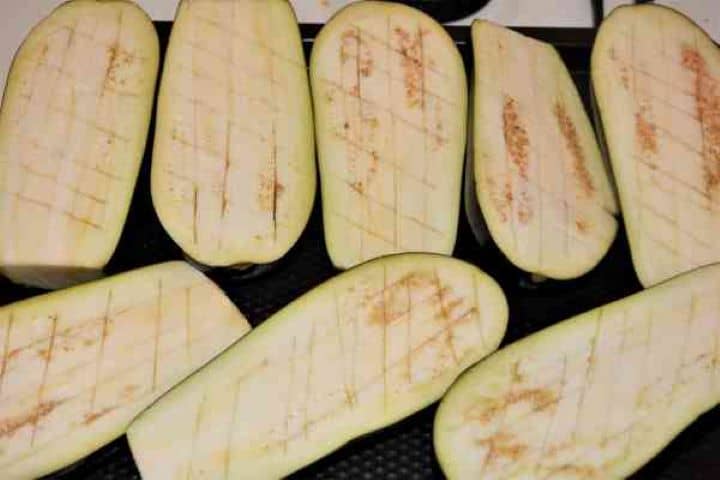 Stuffed Aubergines Recipe-Cut in Two and Notched Aubergines on Baking Pan Sliced aubergine halves with shallow criss-cross notches laid cut-side up on a baking sheet, ready to be drizzled with olive oil.