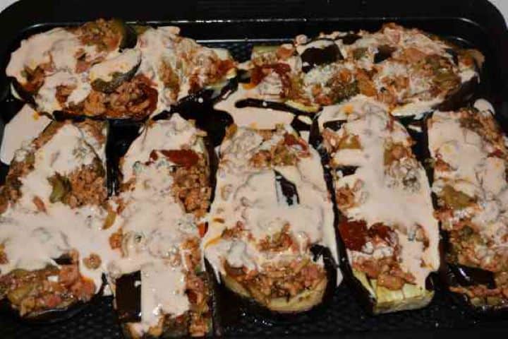 Stuffed Aubergines Recipe-Pouring Cream Sauce Over the Stuffed Aubergines Pouring a rich tomato single cream sauce over savory meat filling inside hollowed-out aubergine shells.