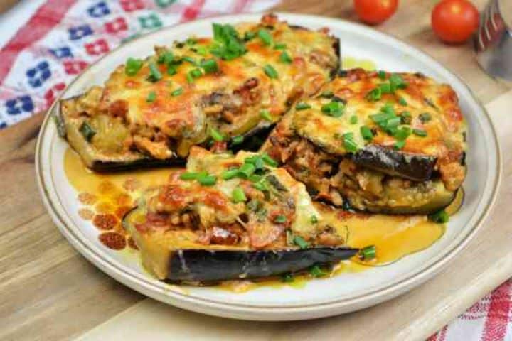 Stuffed Aubergines Recipe-Stuffed Aubergines Served on Plate A plated serving of a smoky pork and bacon stuffed aubergine boat next to a fresh cherry tomatoes ready to eat.