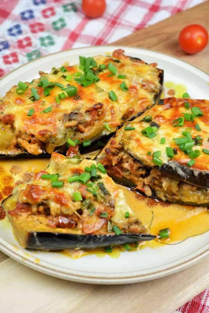 A close-up shot of a juicy pork stuffed eggplant half served on a dinner plate, showcasing the rich meat filling, creamy tomato sauce, and golden melted cheddar cheese top.
