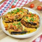 A close-up shot of a juicy pork stuffed eggplant half served on a white dinner plate, showcasing the rich meat filling, creamy tomato sauce, and golden melted cheddar cheese top.