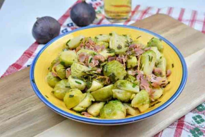 Pan-fried Brussels sprouts with lemon and crispy bacon in a serving bowl next to a cold glass of beer.