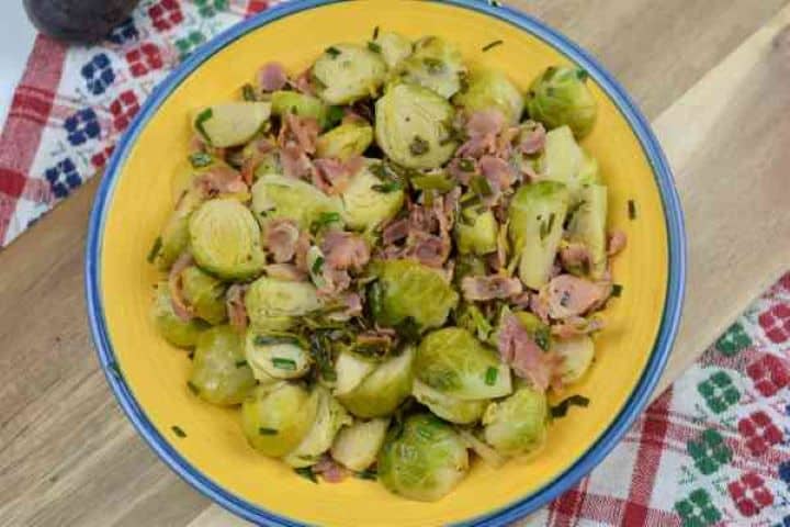 Brussels Sprouts With Lemon-Served in the Yellow Bowl on the Chopping Board Close-up of tender Brussels sprouts tossed with smoked bacon strips and fresh lemon zest.