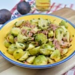 Easy Brussels sprouts with lemon, smoked bacon, and chopped chives served in a yellow bowl on a wooden board.