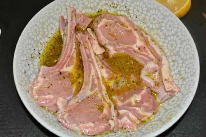 Greek Lamb Chops Recipe-Marinated Lamb Chops Raw lamb chops marinating in olive oil, crushed garlic, fresh lemon juice, and oregano in a shallow white dish.