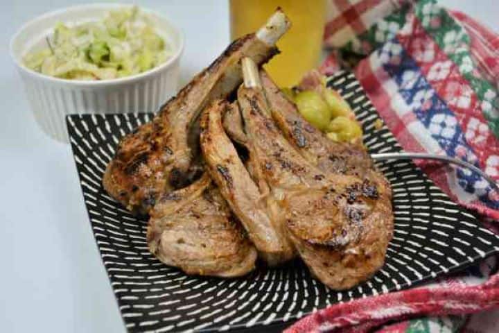 Tender Greek lamb cutlets served with lemon-dressed vegetables and cold beer on a rustic dinner table.