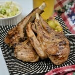 Juicy pan-seared Greek lamb chops garnished with lemon and oregano, served on a black plate with Brussels sprouts and a cold beer.