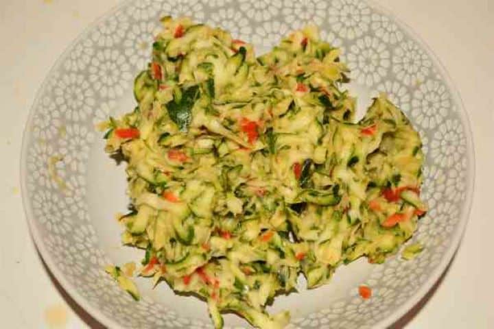 Zucchini Balls Recipe-Squeezed Grated Zucchini and Kapia Pepper on the Plate Tightly squeezed grated zucchini, leek, and red pepper drained of excess water on a plate.