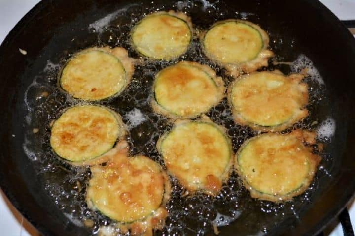 Battered Fried Zucchini-Fried Battered Zucchini Slices in the Frying Pan Golden beer battered zucchini slices bubbling and frying evenly in a pan.