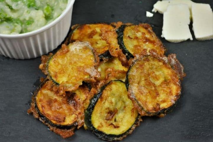 Battered Fried Zucchini-Served on Slab With Garlic Cream and Cheddar Cheese Platter of golden beer battered fried zucchini served on a black stone slab with garlic dip and cheese.