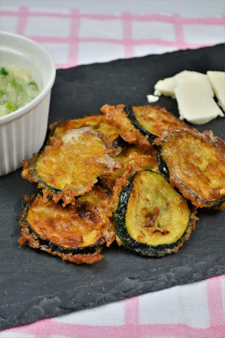 Battered Fried Zucchini-Served on Slab With Garlic Cream and Cheddar Cheese Golden beer battered fried zucchini slices served on a plate with creamy garlic dip and cheddar cheese.