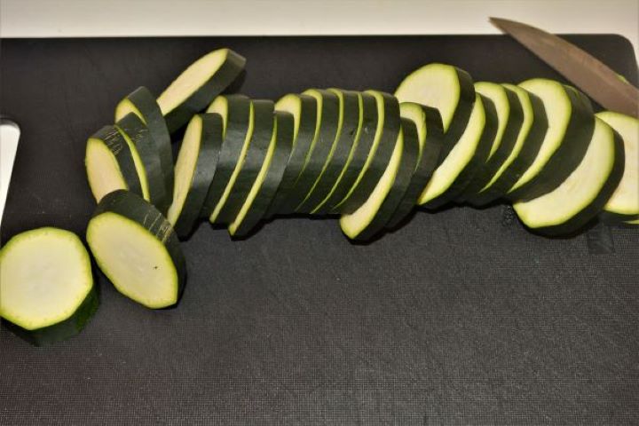 Battered Fried Zucchini-Sliced Zucchini on the Chopping Board Fresh green zucchini sliced into half-inch thick rounds on a black chopping board.