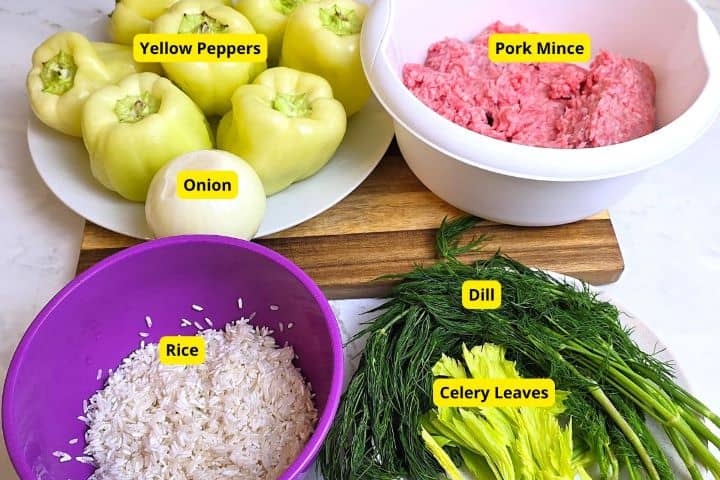 Hungarian Stuffed Peppers-Six Peppers and One Onion on the Chopping Board Yellow Peppers, Pork Mince, Rice, Dill, and Celery Leaves on the Table