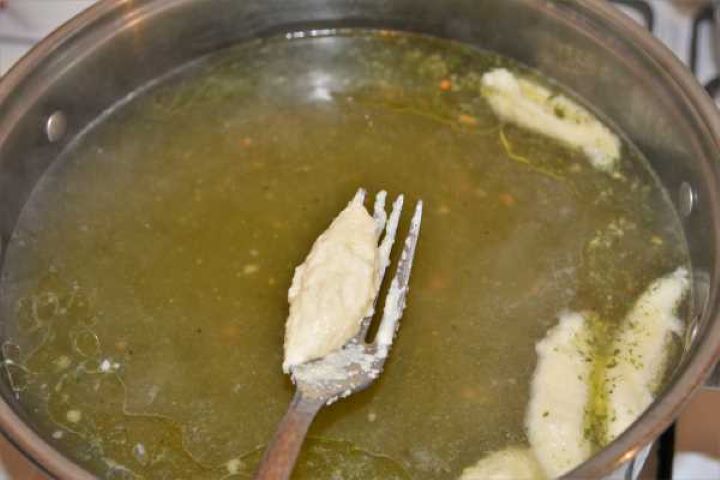 Semolina Dumplings Soup-Adding Dumplings in the Soup With a Fork Dropping spoonfuls of raw semolina dumpling batter into gently simmering broth.