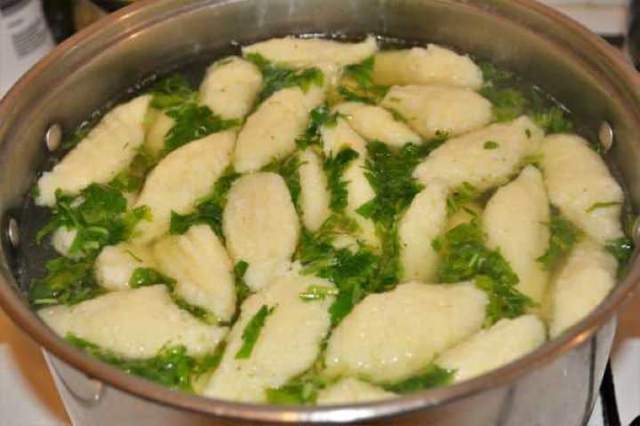 Semolina Dumplings Soup-Ready to Serve in the Pot Golden semolina dumplings soup sprinkled with freshly chopped flat-leaf parsley in the pot.