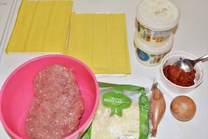 Turkey Lasagna With White Sauce-All Ingredients on the Table Ingredients for turkey lasagna including minced turkey, fresh lasagna sheets, cheese sauce, and mozzarella on a kitchen table.