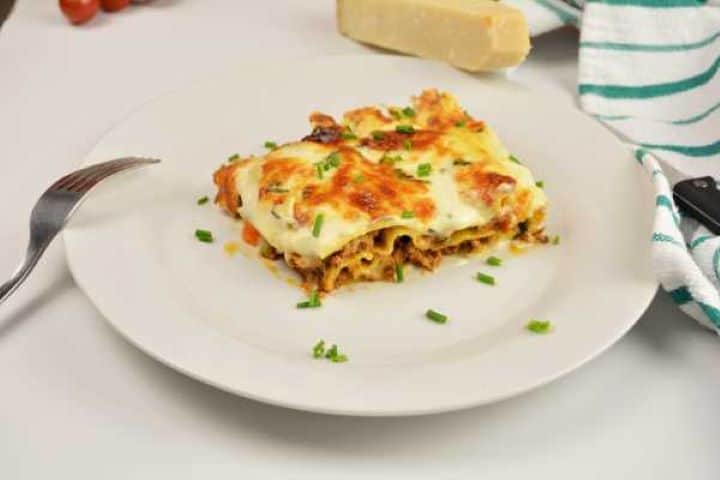 Turkey Lasagna With White Sauce-Lasagna Slice Served on Plate With Chopped Chives on Top Warm square slice of baked turkey lasagna showing distinct pasta and meat layers topped with chives.