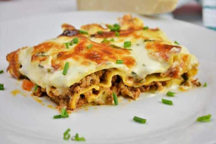 Turkey Lasagna With White Sauce-Lasagna Slice Served on Plate With Chopped Chives on Top Close-up of a fork taking a bite of tender turkey lasagna showing creamy white cheese sauce and seasoned mince layers.