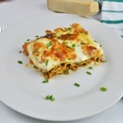 Slice of creamy turkey lasagna with white sauce garnished with chopped chives on a plate.