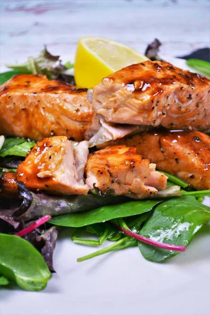 Serve A close-up view of perfectly flaky air fryer teriyaki salmon served on plate with salad Mix and fresh lemon.