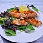 A close-up view of perfectly flaky air fryer teriyaki salmon served on plate with salad mix and lemon slice.