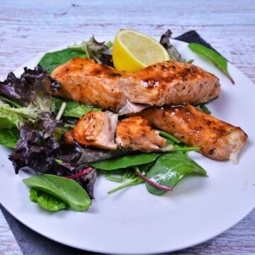 A close-up view of perfectly flaky air fryer teriyaki salmon served on plate with salad mix and lemon slice.
