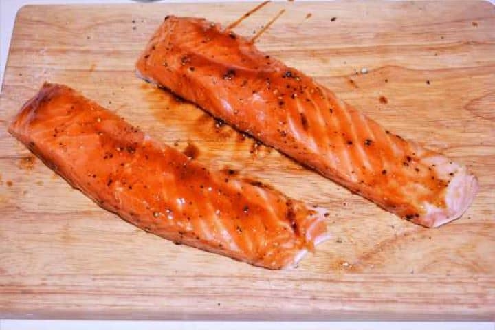 Teriyaki Glazed Salmon Fillets Raw salmon fillets seasoned with salt and pepper and brushed with a thick layer of dark teriyaki sauce glaze on chopping board.