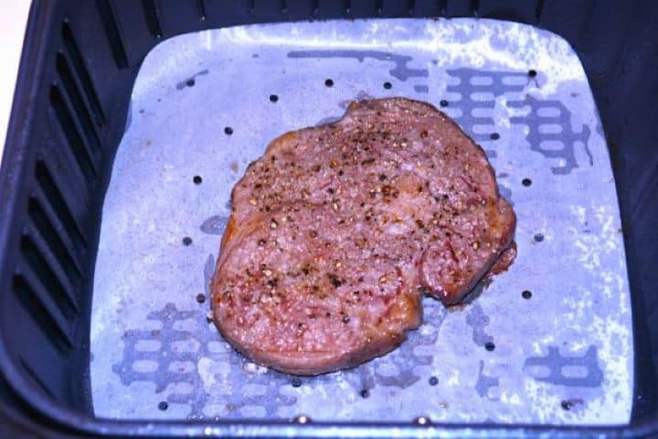 Ribeye Steak in Air Fryer-Cooked Ribeye Steak in the Air Fryer Basket Golden-brown cooked ribeye steak resting on parchment paper inside the air fryer basket.
