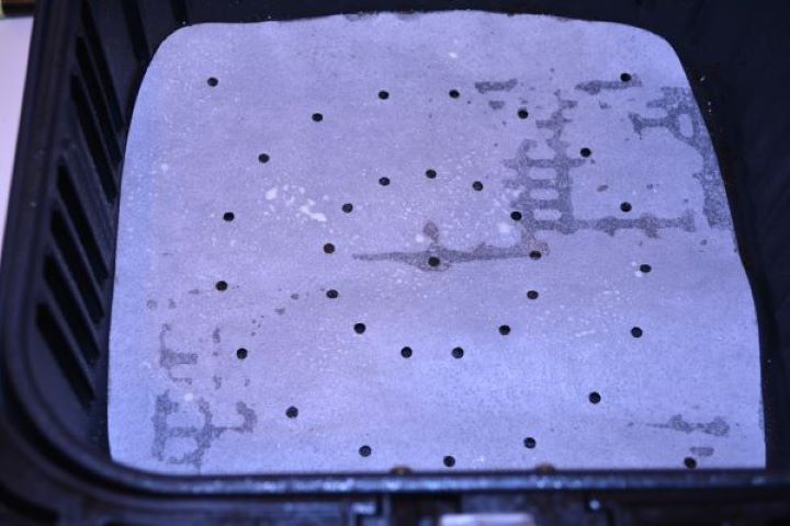 Preheated Cosori air fryer basket lined with parchment paper and lightly sprayed with olive oil.